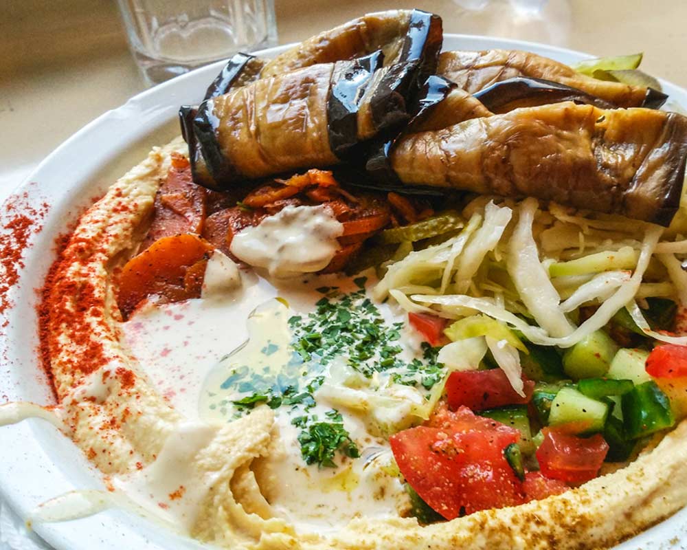 piatto di verdure miste con hummus, melanzane, pomodori, carote e verza budapest vegana e senza glutine