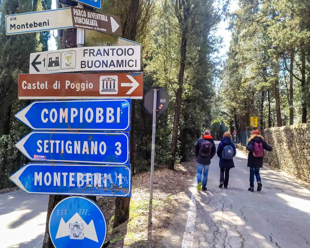 indicazioni stradali e tre persone che camminano verso il castello di vincigliata