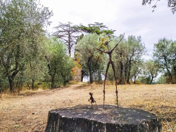 instalazione artistica su un tronco d'albero circondato da oliveti e cappella di zano in fondo